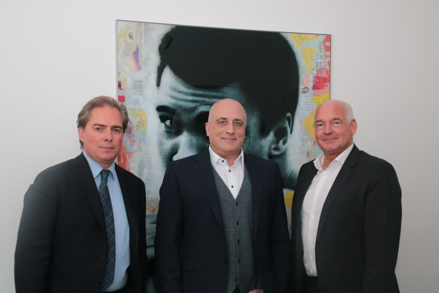 Drei männliche Führungskräfte in Business-Kleidung vor einem modernen Kunstwerk.